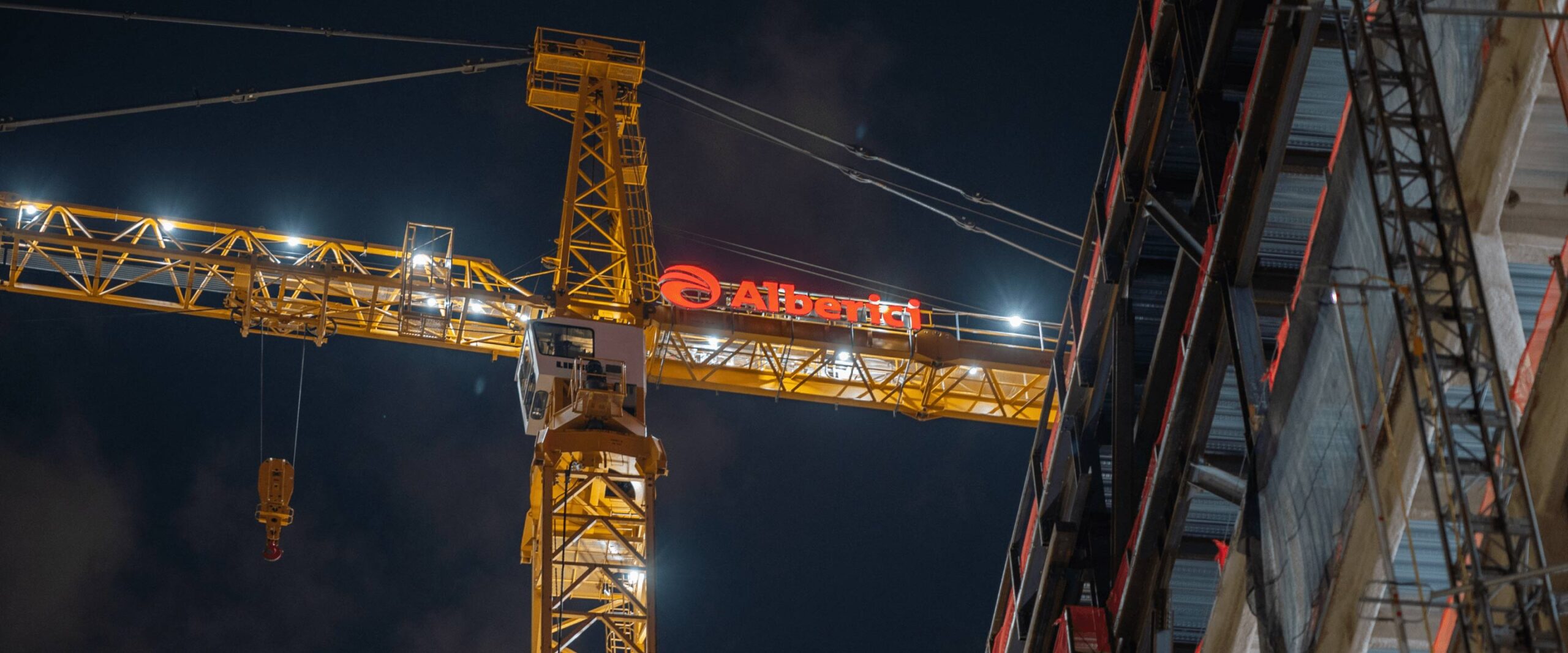 A construction crane, lit up at night, with the Alberici branding